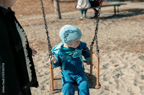 A little boy sits on an iron swing. The kid is riding on a swing in the park