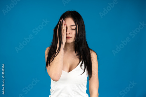 Front view of woman in casual attire covering eye with hand isolated on blue background