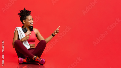Cheerful fitness model sitting on floor, pointing at free space