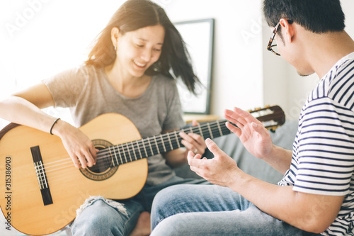 couple playing acoustic guitar,sing folk song together sitting on sofa at home.concept for happy moments of young lovers,family.music and art therapy for people with stress.asian man,women relax time
