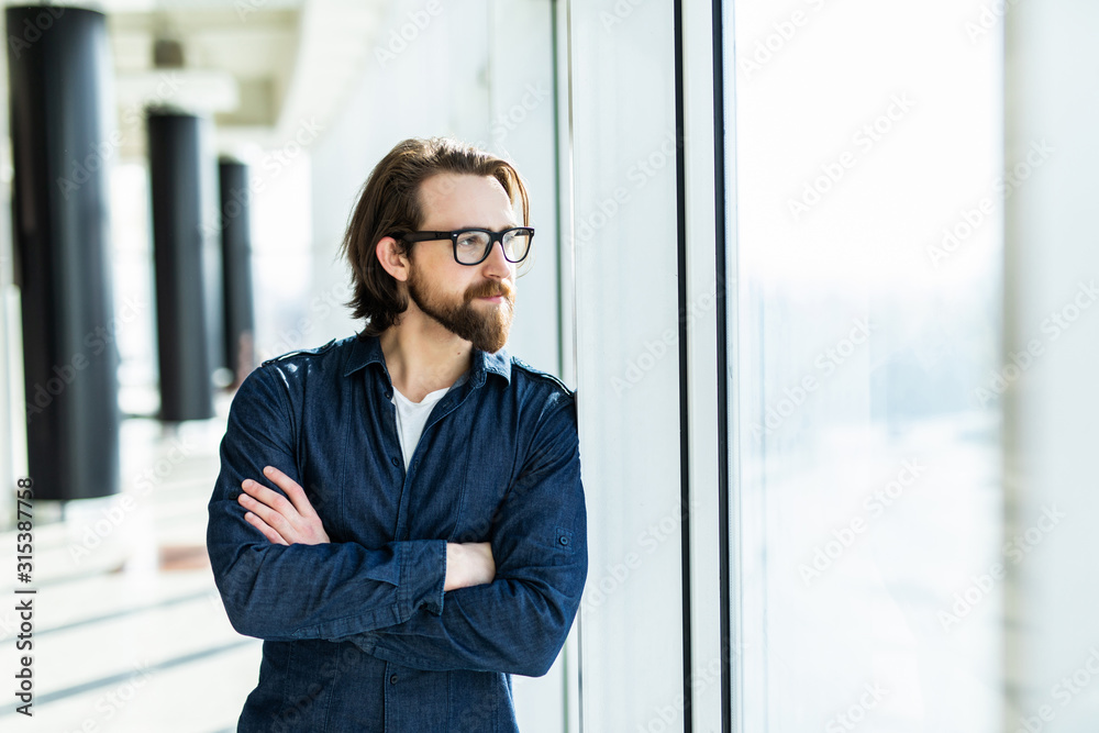Handsome confident employee in a glasses standing in the office near the table holding his hands crossed and smiling. Handsome confident employee in a glasses standing in the office near the table holding his hands crossed and smiling.