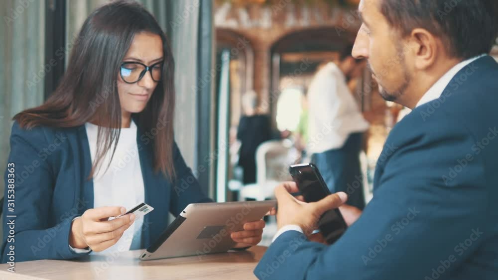 Two businesspeople in deep blue suits are working. Man is giving his partner a shopping card and handshake. Woman is smoling. Close up. Copy space. Two businesspeople in deep blue suits are working. Man is giving his partner a shopping card and handshake. Woman is smoling. Close up. Copy space.