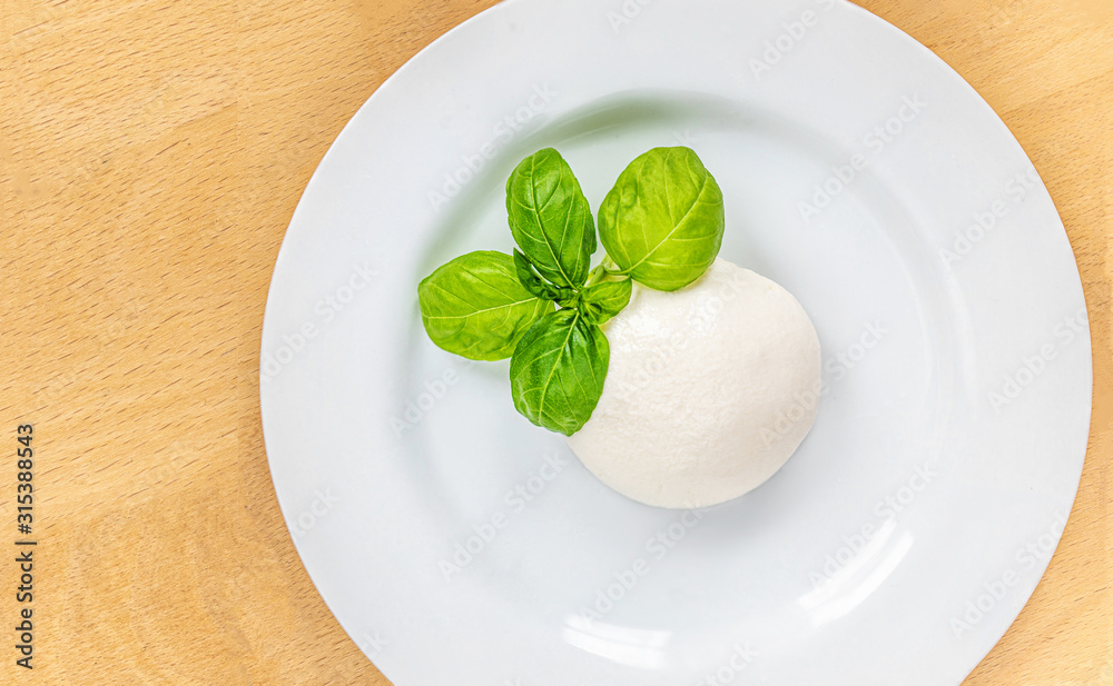 Traditional Italian Mozzarella cheese and basil leaf on white plate over wood table. Traditional Italian food . Traditional Italian Mozzarella cheese and basil leaf on white plate over wood table. Traditional Italian food .