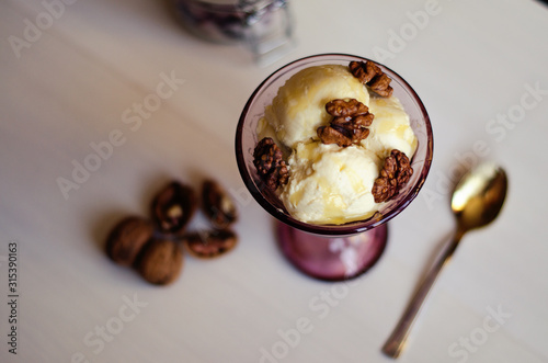 Creamy ice cream with honey and walnuts. Served in a bowl with ice cream, garnished with walnuts and honey. On the table is a spoon and a walnut. Close-up. Copy space
