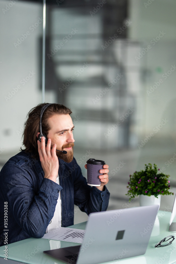 Smiling young call center man operator in headset working with laptop in office