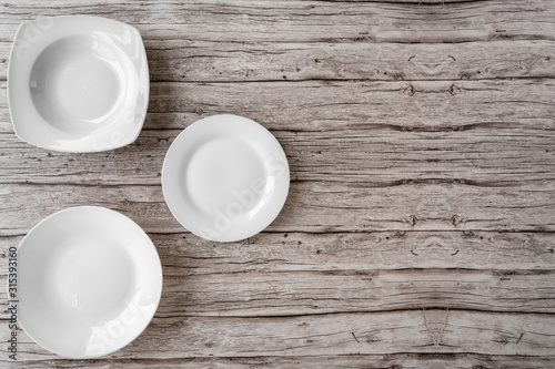 White empty ceramic plates in different shapes on old wooden background of a table. Plates clean for kitchen, porcelain dishware. Top view with copy space for text.