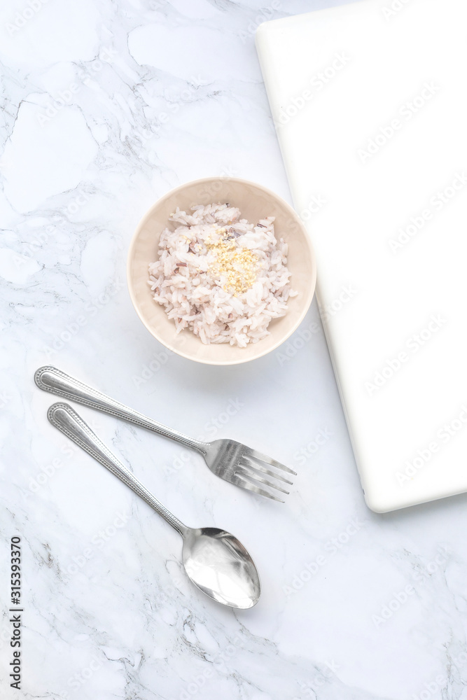 Boiled white rice in a cup with a spoon and white computer notebook with copy space top view - Flat lay Boiled white rice in a cup with a spoon and white computer notebook with copy space top view - Flat lay