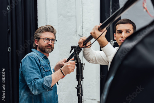 selective focus of handsome men holding light stand in photo studio