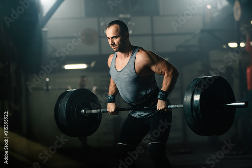Fototapeta Naklejka Na Ścianę i Meble -  Athletic man making an effort while weightlifting on strength training in a gym.