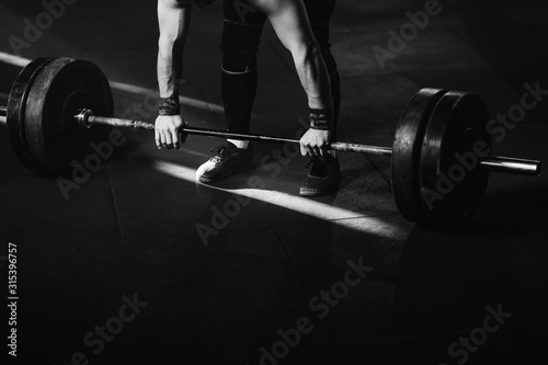 Unrecognizable sportsman exercising with barbell in a gym.