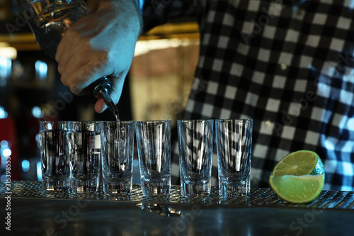 Bartender pouring Mexican Tequila into shot glasses at bar counter  closeup