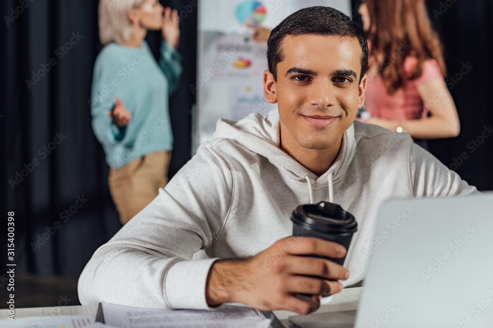 selective focus of happy art director holding paper cup while using laptop selective focus of happy art director holding paper cup while using laptop