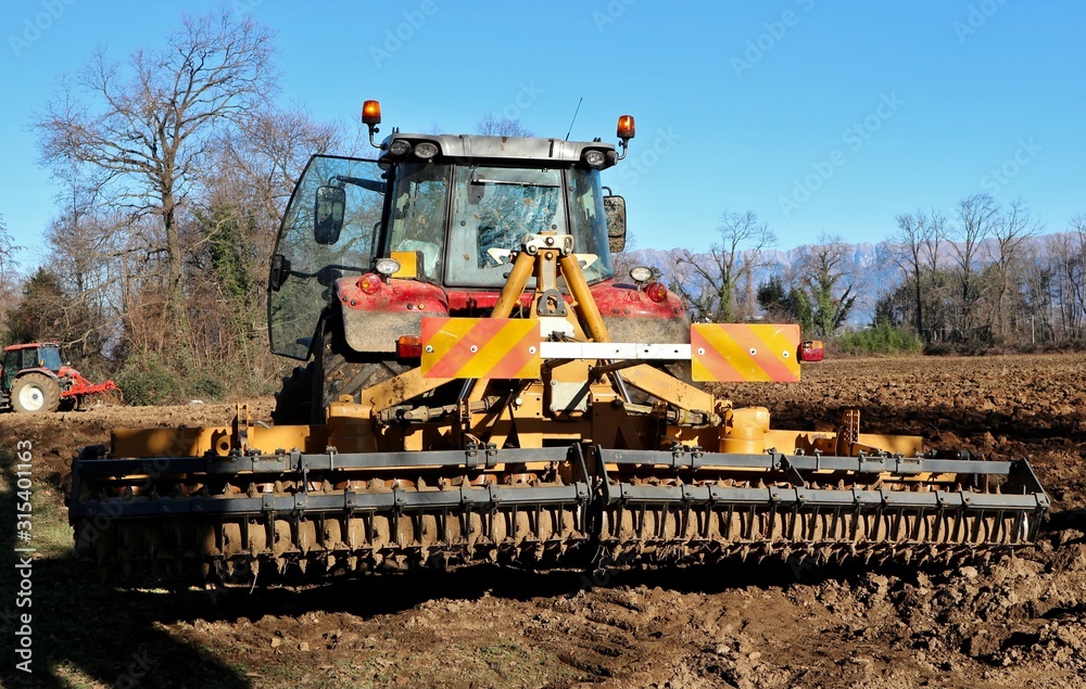 Rotary harrow and compactor, behind a tractor, at work on a field in winter to prepare the soil Rotary harrow and compactor, behind a tractor, at work on a field in winter to prepare the soil