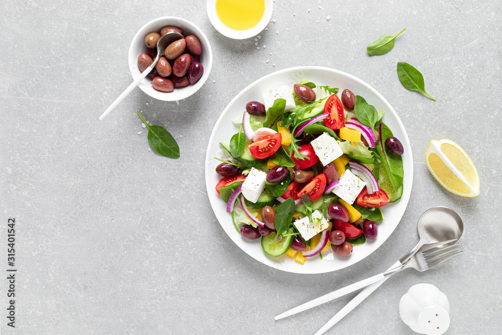 Greek salad with greens, olives and feta chesse on a white plate, top view Greek salad with greens, olives and feta chesse on a white plate, top view