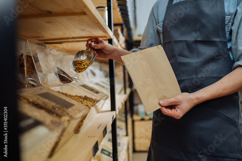 Mixed race male worker shop assistant filling paper bag with oat granola in bulk products in dispensers and food available at zero waste shop. photo