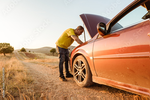 Man examining broken car in countryside photo