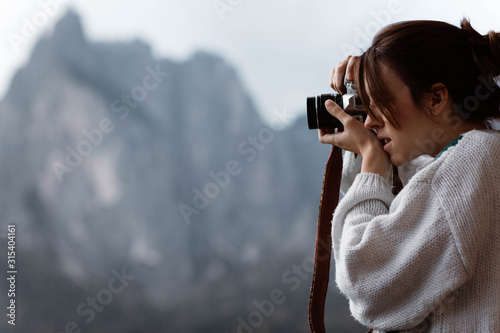 Side view of woman traveler in casual plaid shirt taking photo from opened window of nature at Dolomites mountains, Italy