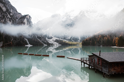 Wooden house on stilts and boats on nebulous lake with reflection of powerful Dolomites mountains at Italy photo