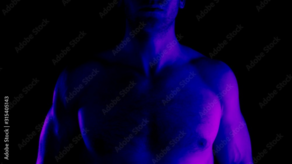 The male body is lit by a flickering fashionable color. Athlete's naked body on a black background. Flashing light and a man. The male body is lit by a flickering fashionable color. Athlete's naked body on a black background. Flashing light and a man.