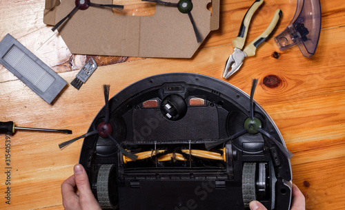 Repairing a robot vacuum cleaner. Hands of the repairman hold the device