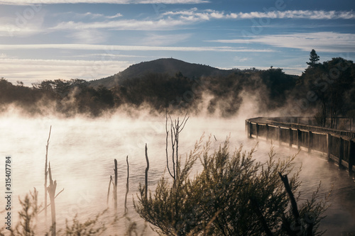 Mysterious foggy lake near woody bridge with big mountains and blue sky on background at Rotoura photo