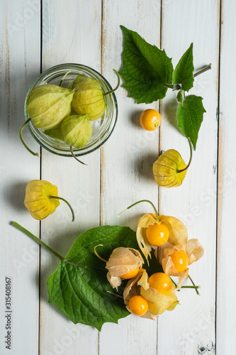 Physalis fruit (Physalis peruviana) also called uchuva, cape gooseberry or gold berries, native of Peru, on a wooden white board with leaves. photo