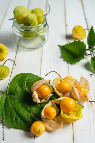 Physalis fruit (Physalis peruviana) also called uchuva, cape gooseberry or gold berries, native of Peru, on a wooden white board with leaves.
