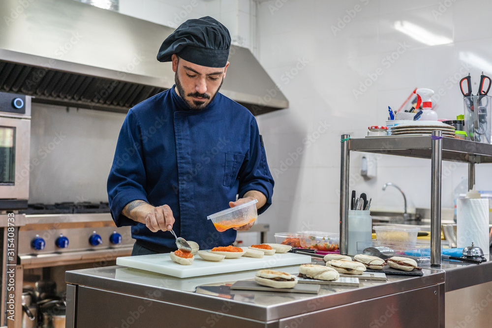 Professional cook in uniform and hat preparing gourmet sandwiches with red caviar while working in restaurant kitchen Professional cook in uniform and hat preparing gourmet sandwiches with red caviar while working in restaurant kitchen