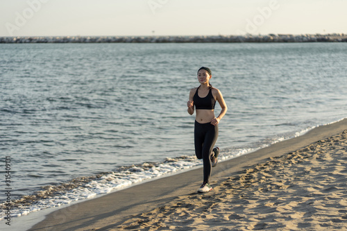 Motivated young female athlete in active black wear and sneakers jogging along sandy empty seashore photo