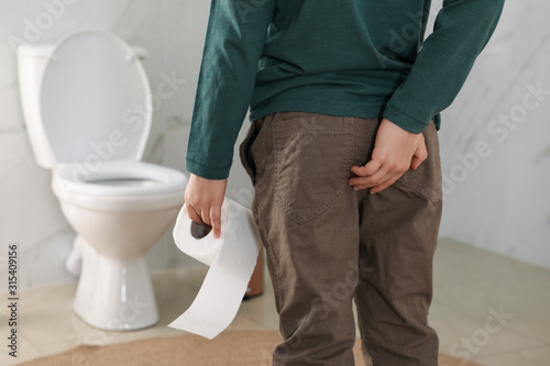 Boy with toilet paper suffering from hemorrhoid in rest room, closeup