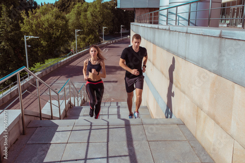 A young and athletic couple, a man and a woman, run in summer in city on morning on stairs. Active healthy youth lifestyle. Sportswear, afternoon in city.