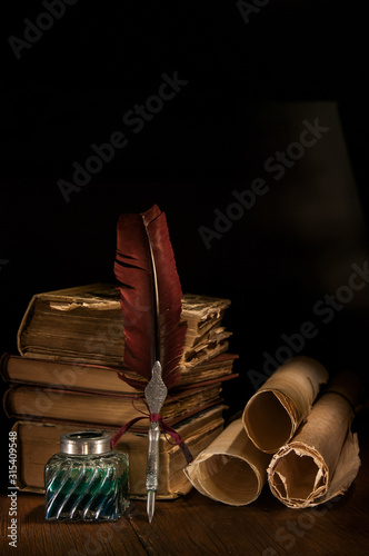 Quill pen and a rolled papyrus sheet on a wooden table with old books, warm effect