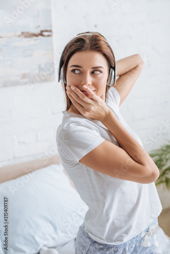 young woman covering mouth and listening music at home
