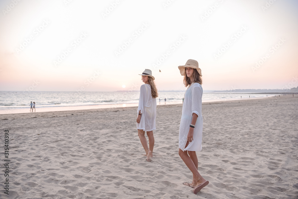 Smiling girlfriends in summer clothes barefoot in water on beach