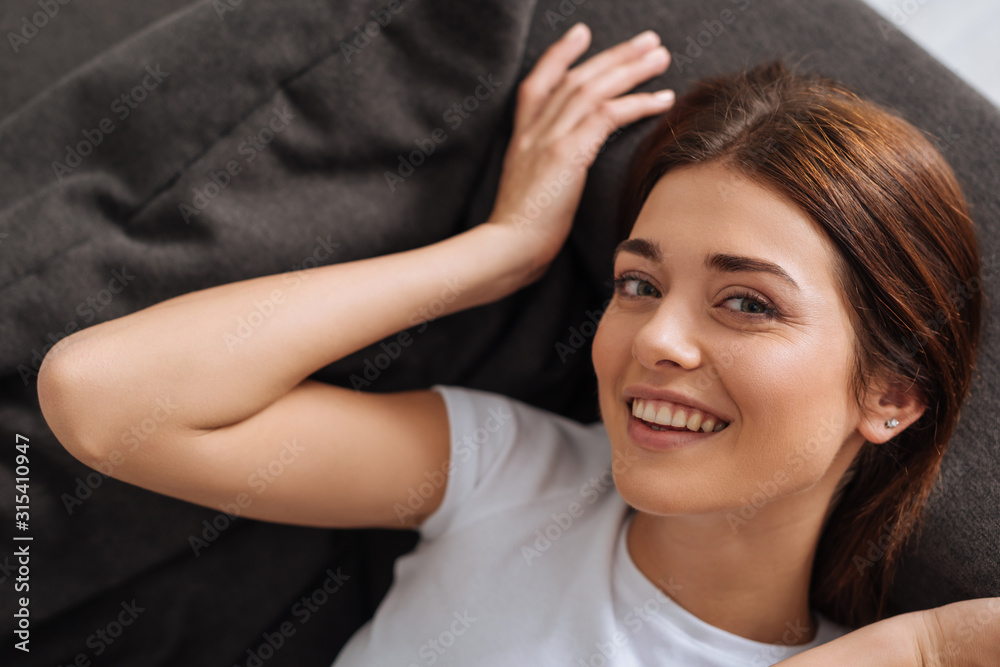 top view of happy woman looking at camera while resting on sofa in living room top view of happy woman looking at camera while resting on sofa in living room