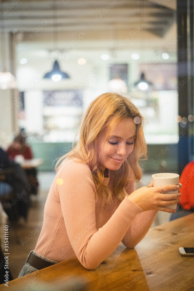 Throughout a glass view of young woman having cup of coffee at table in cafe