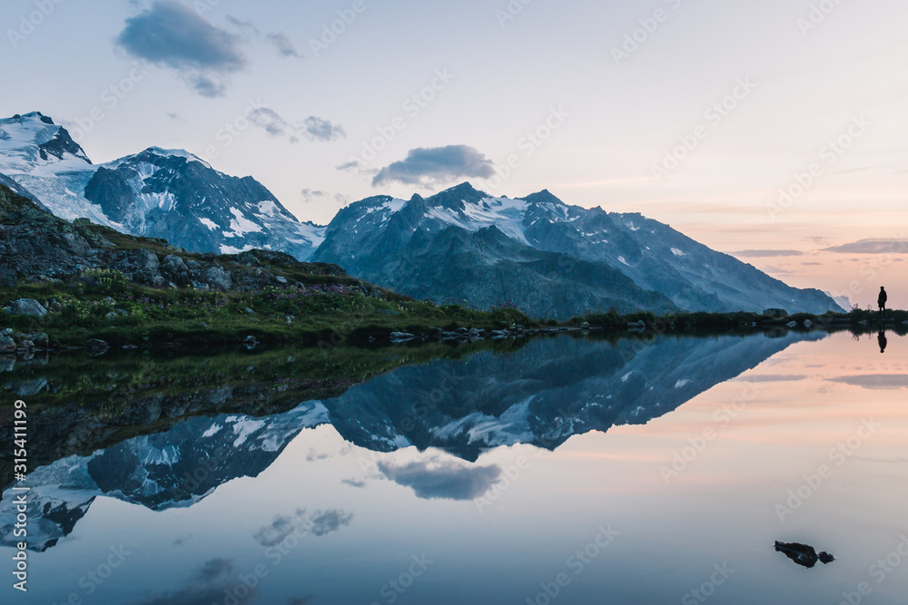 Silhouette standing at calm lake coast in snowy mountains reflecting sky in Switzerland Silhouette standing at calm lake coast in snowy mountains reflecting sky in Switzerland
