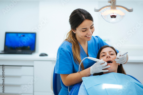 Dentist and assistant examining mouth of patient in chair with tools