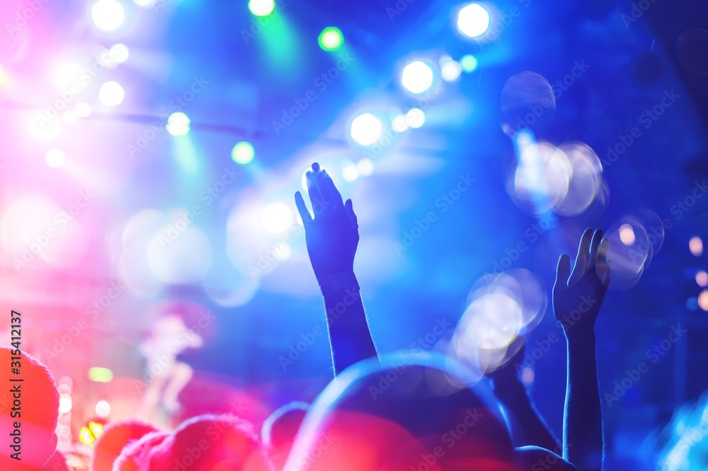 Hands raised at a music festival and lights streaming down
