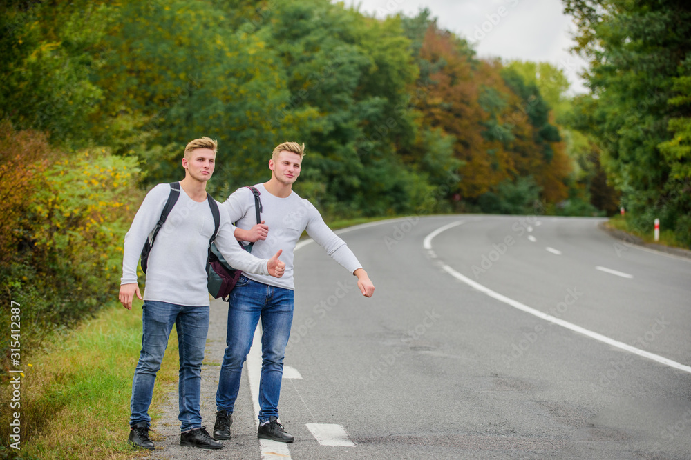 men backpacks walking together by road. twins walking along road. Adventure and discovery. Man with backpack hitchhiking on road. Summer vacation. Tourist traveler travel auto stop. Budget travelers men backpacks walking together by road. twins walking along road. Adventure and discovery. Man with backpack hitchhiking on road. Summer vacation. Tourist traveler travel auto stop. Budget travelers