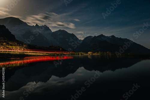 Dramatic breathtaking landscape of red-lit shore and dark tranquil water reflecting cloudy sky and mountains in evening in Switzerland