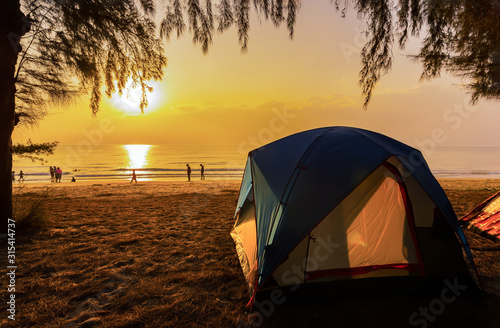 The image of a camping tent and activity on the beach in the morning with golden sky and sunrise. Hat Wannakon, a beach filled with pine trees in Thailand.