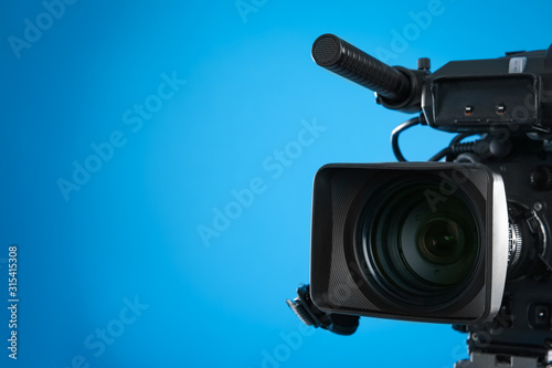 Professional video camera on blue background, closeup. Space for text