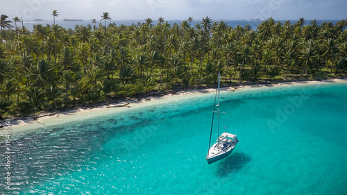 Sailing Yacht in San Blas Islands, Panama. A beautiful Aerial Shot of a white Sailboat anchored in a Blue Lagoon in front of a paradisiacal Tropical Caribbean Island overgrown with green Palm Trees.