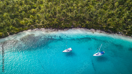 San Blas Islands, Panama - Aerial Drone Top Down View of two Sailing Yachts anchored in Turquoise Water right next to perfect White Sand Beach of Caribbean Tropical Island full of green Palm Trees.