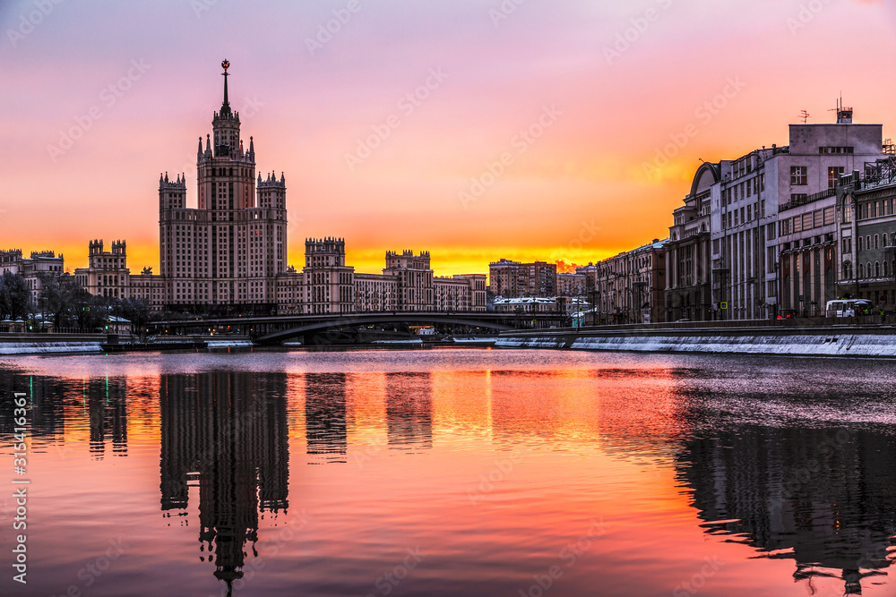 Bright colorful winter dawn on Moscow-a river with reflection in the water of the buildings of Kotelnicheskaya and Raushskaya embankments. Moscow, Russia