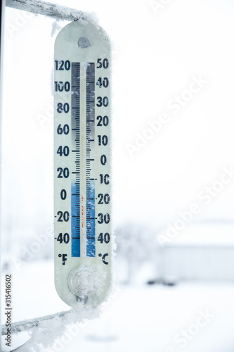 A vertical large outdoor temperature gauage surrounded by frost along outside edges on a cold winter day photo