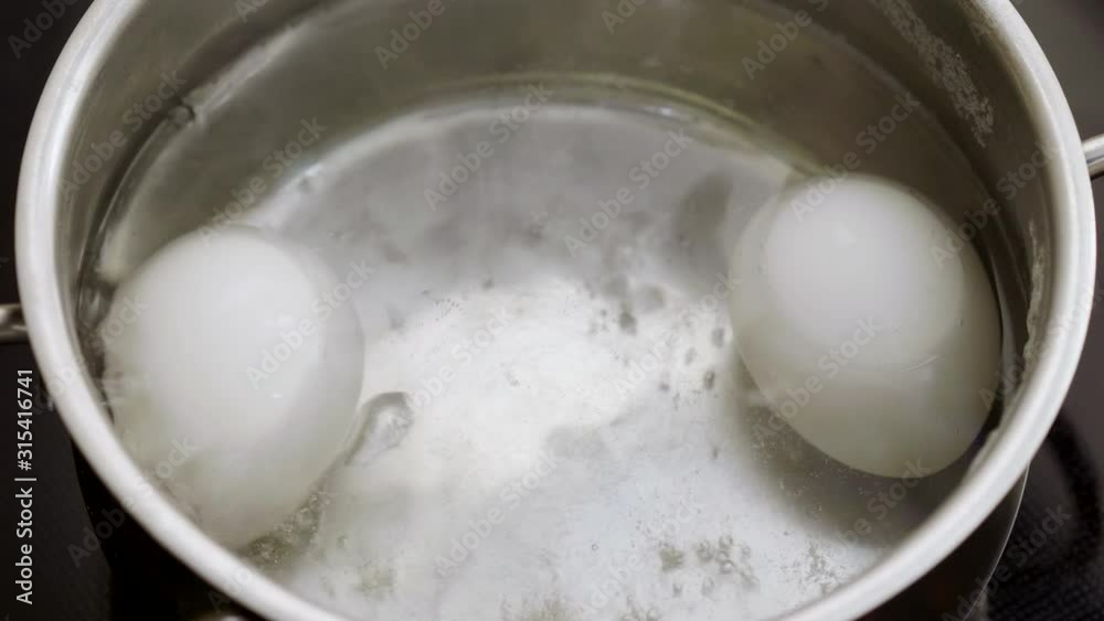 Close-up of two white chicken eggs in a pan of boiling water. 4K