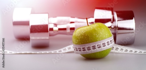 Tableau sur toile Dumbbell with green apple and tape measure on desk