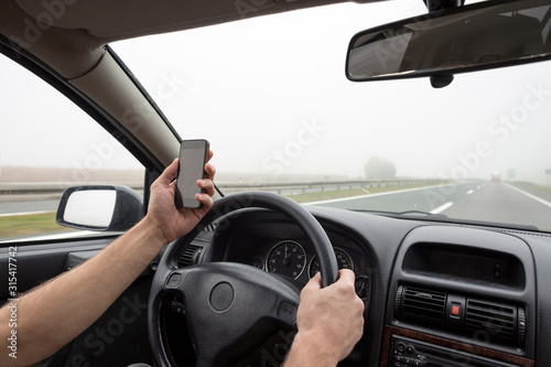 Use of smartphone in car. Man using phone while driving in fog on highway. © MexChriss